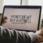 computer screen with quote 'money doesnt buy happiness' - person with money and a human hand holding it.